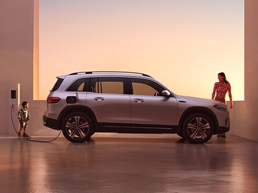 EQB totalmente eléctrica de Mercedes-Benz, recargando la batería en una estación de carga. También se ve a un niño y una mujer cerca de la EQB.