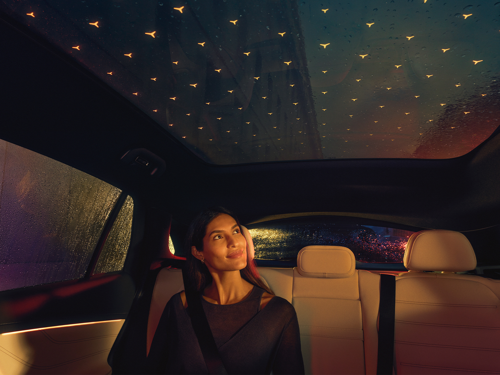 Interior del Mercedes-Benz GLC mostrando su techo panorámico iluminado por estrellas Pasajero sentado en un Mercedes-Benz GLC bajo un techo panorámico con luces de estrellas radiantes