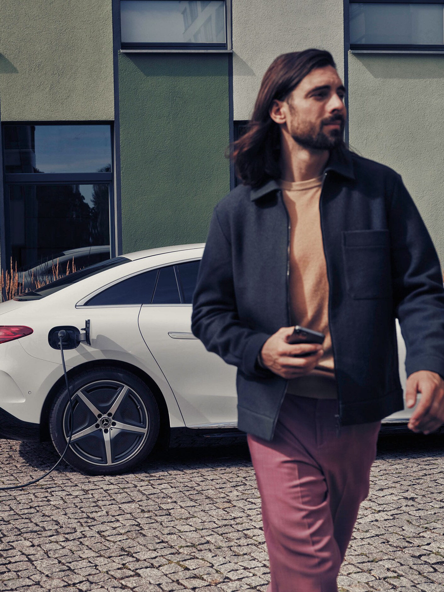 Una hombre camina junto a un Mercedes-Benz EQS blanco en carga