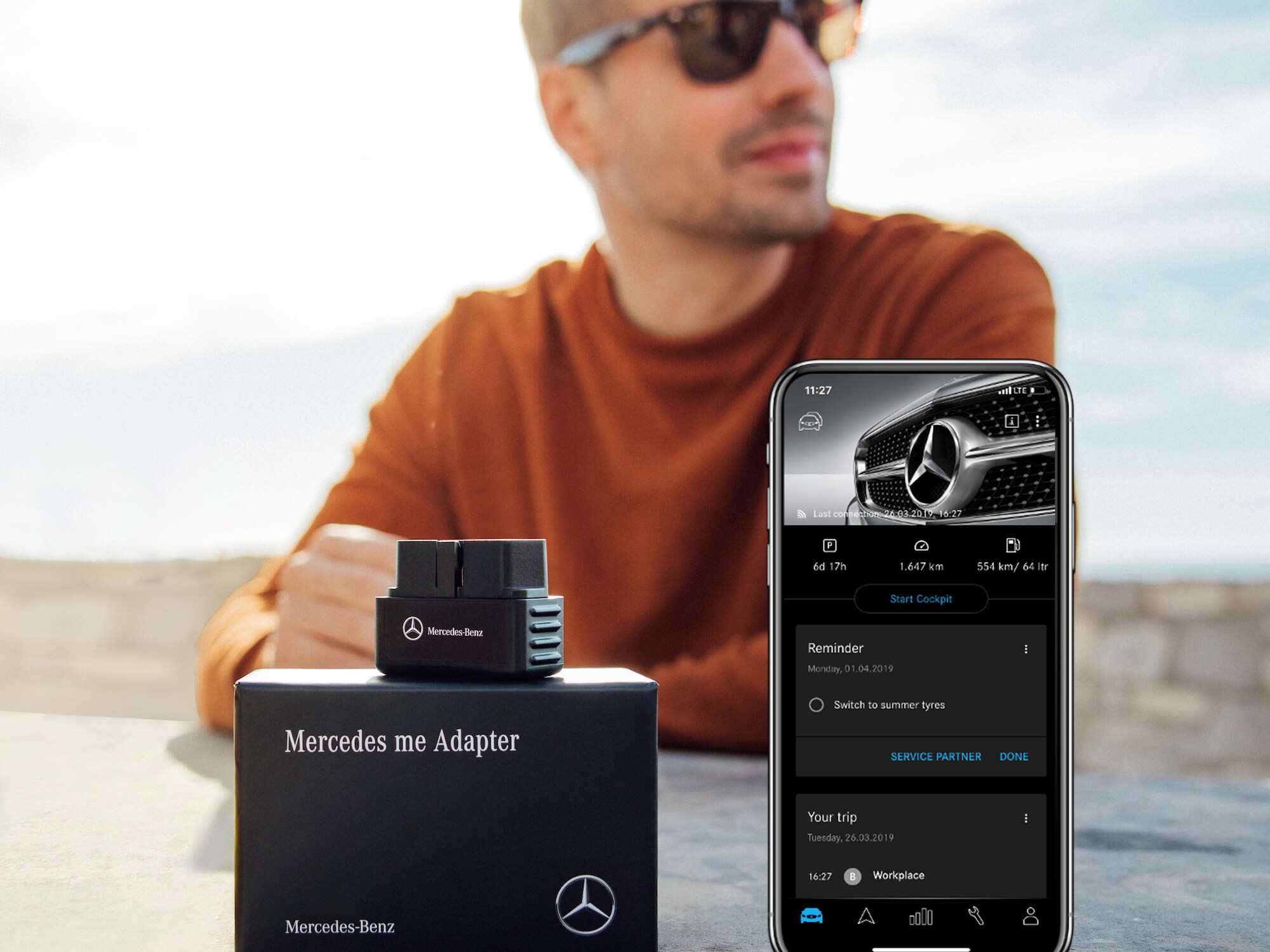 Un hombre muestra el Mercedes me Adapter y la Mercedes me App en su smartphone.