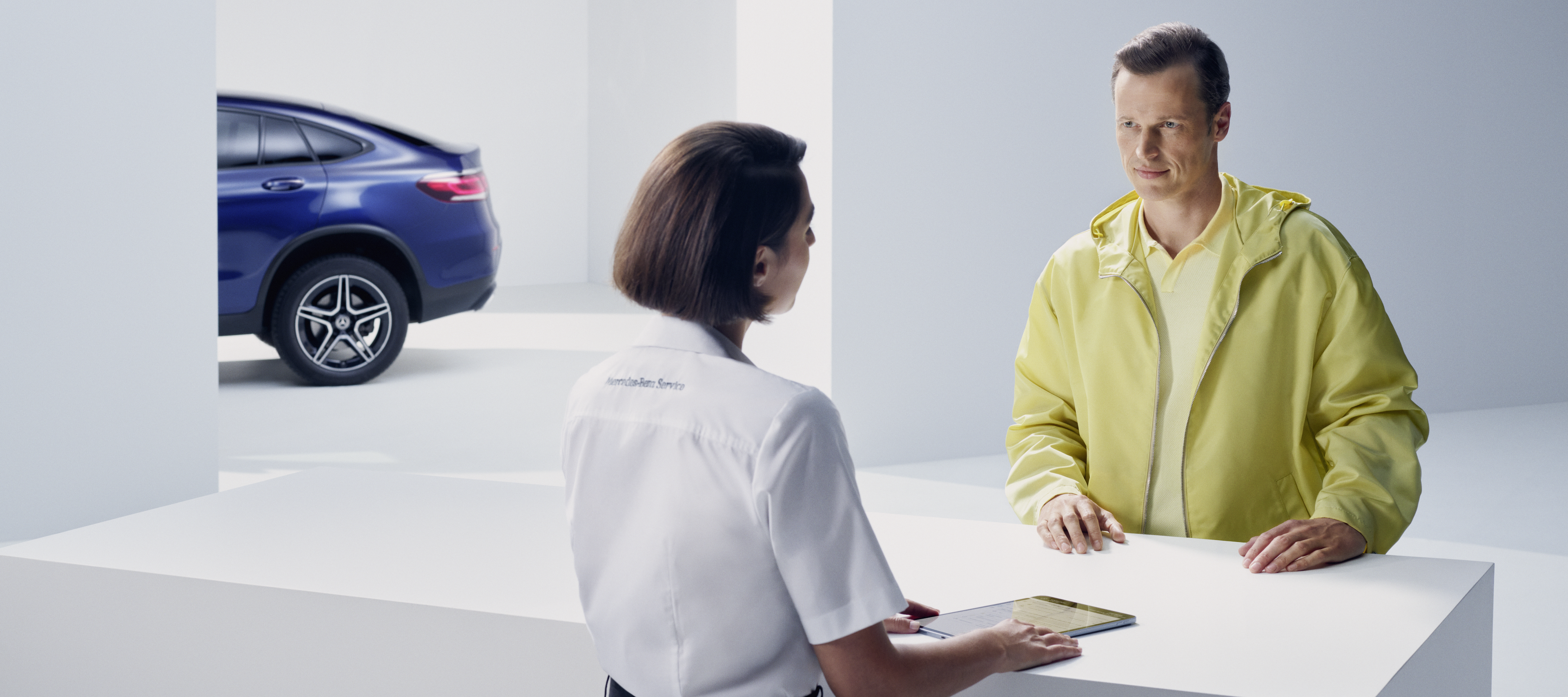 Llamada a taller de Mercedes-Benz | Mercedes-Benz Un cliente se apoya en el mostrador mientras espera a que una empleada de Mercedes-Benz le atienda.