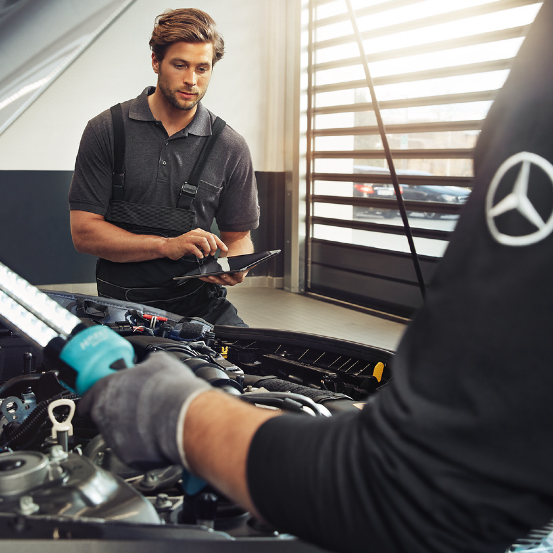 Refacciones originales Mercedes-Benz Dos técnicos de Mercedes-Benz examinan el compartimento del motor de un vehículo.