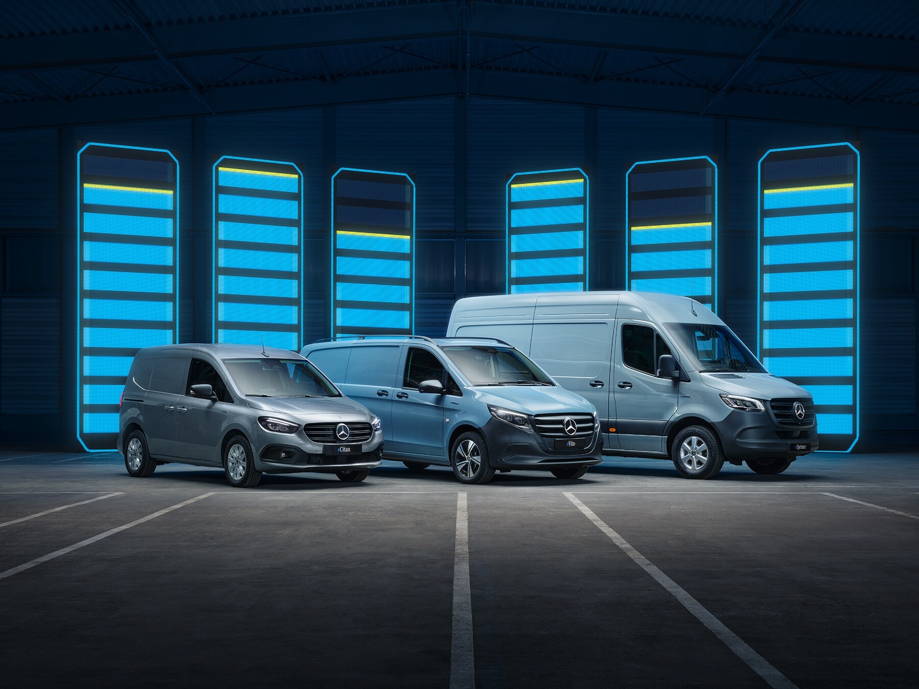 Una serie de vanes eléctricos de Mercedes-Benz se muestra en un depósito futurista con barras de recarga iluminadas