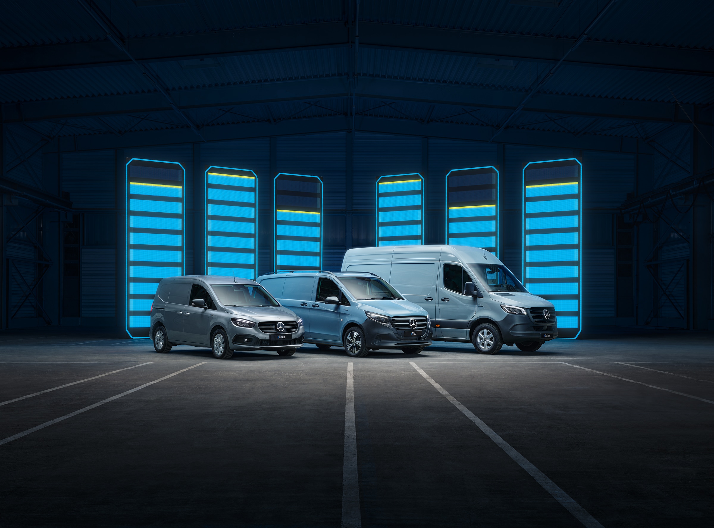 Gama de vanes eléctricos de Mercedes-Benz | Historia de los vehículos industriales | Mercedes-Benz Una serie de vanes eléctricos de Mercedes-Benz se muestra en un depósito futurista con barras de recarga iluminadas