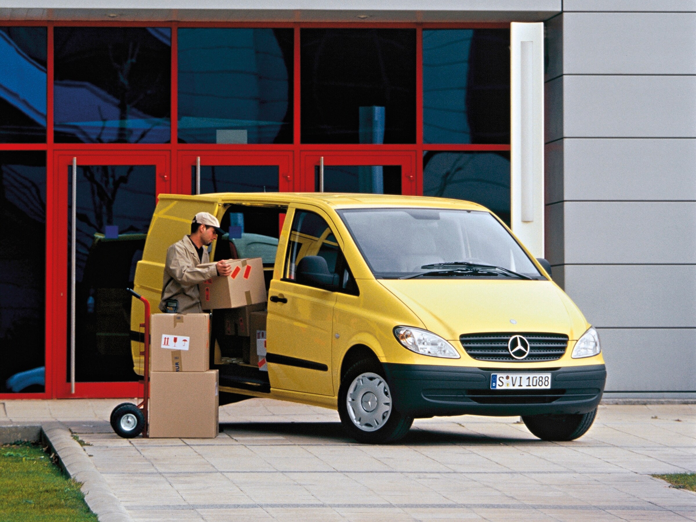 Un Mercedes-Benz Vito amarillo aparcado frente a un edificio, con un trabajador descargando paquetes