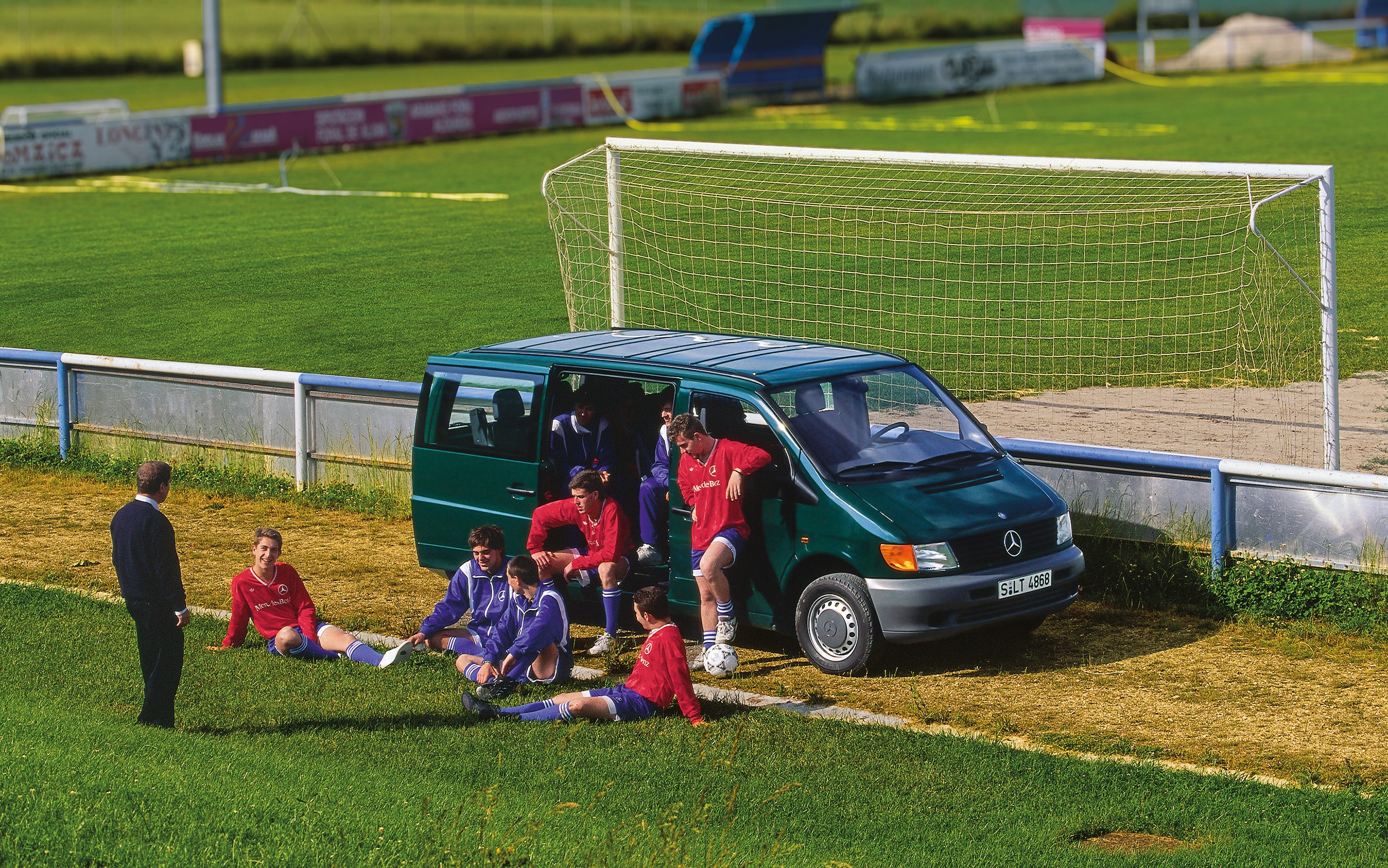 La primera generación de Mercedes-Benz Vito | Historia de los vehículos industriales | Mercedes-Benz Una Vito de primera generación aparcada junto al campo de fútbol, con los jugadores del equipo cerca