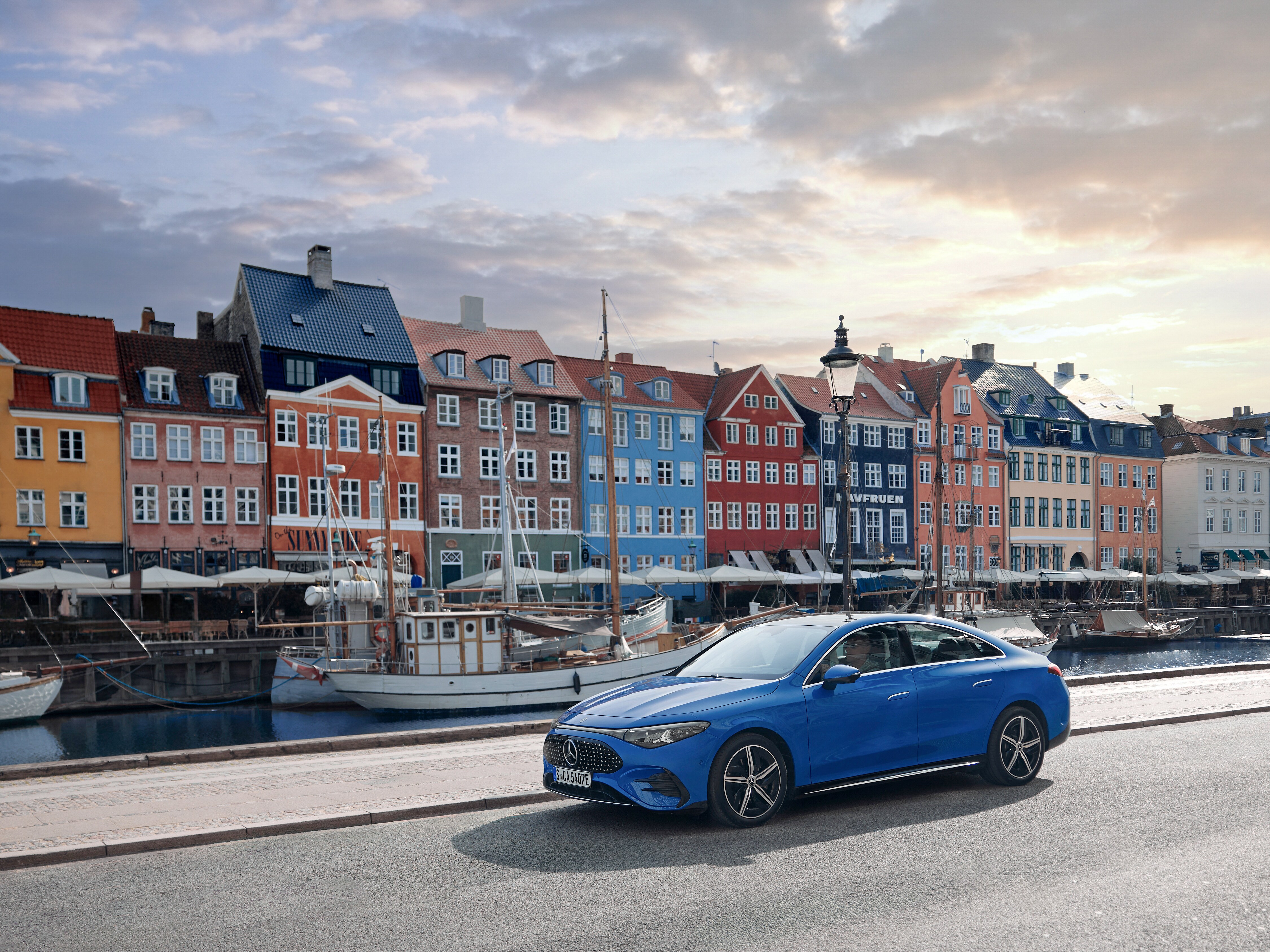 El totalmente nuevo CLA eléctrico color azul con fondo colorido de construcciones y lago con barcos.